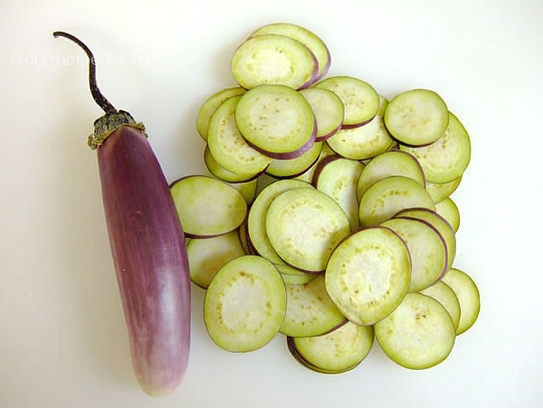 Die violetten Mini-Auberginen mit der Aufschnittmaschiene oder einem scharfen Messer in dünne Scheiben schneiden