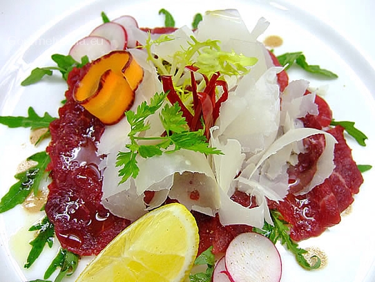 Carpaccio of beef with lemon oil and parmesan flakes on rocket bed