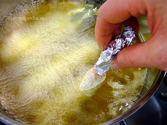 Die panierten Spargeln in das heiße Öl eintauchen