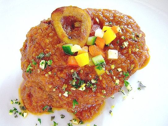 Kalbsstelzenschnitte mit Sauce übergießen und mit Gremolata und Gemüsewürfel bestreuen