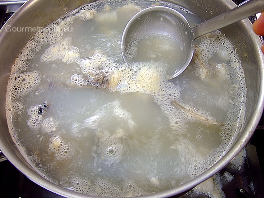 Die Fischreste in Wasser in einem Topf zum Kochen bringen und aufsteigenden Schaum abschöpfen