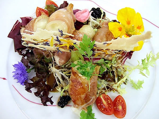 Grilled tomino cheese in raw ham on fancy salad with blossoms and balsamic caviar