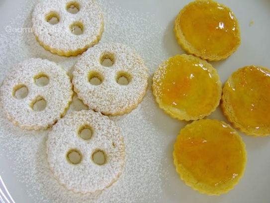 Einen Teil der Böden mit der Aprikosenmarmelade bestreichen und ebenso viele Deckel mit Staubzucker bestreuen