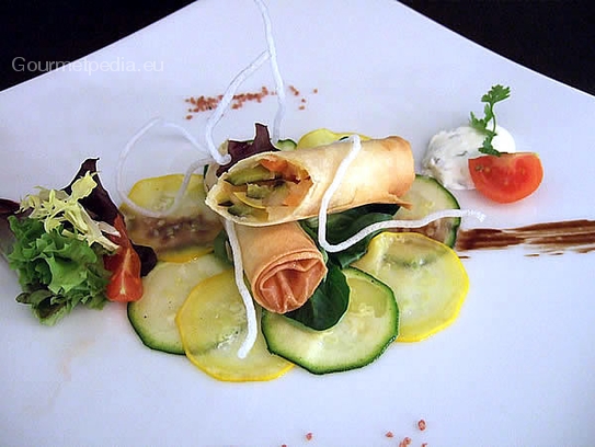 Crispy spring rolls stuffed with spicy king prawns and vegetables on courgettes carpaccio and sour cream sauce