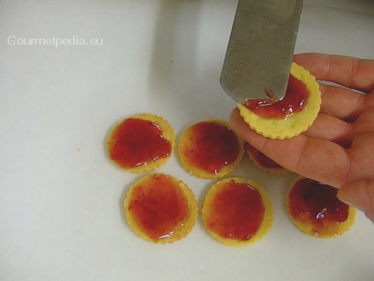 Die Plätzchen auskühlen lassen und die Hälfte mit Erdbeermarmelade bestreichen