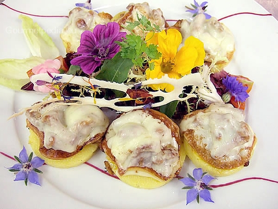 Polenta cakes with mushrooms and cheese au gratin, fancy salad and edible garden flowers