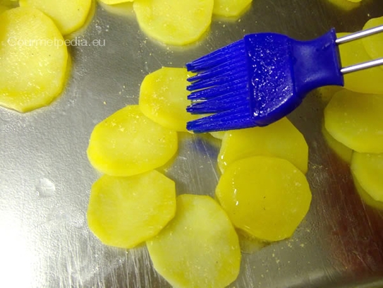 Die Kartoffelscheiben auf einen gefetteten Backblech in einem Kreis aneinander legen und mit geklärter Butter bestreichen