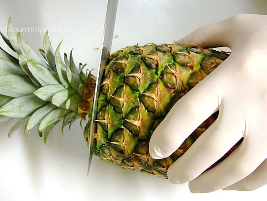 Mit einem Messer den Kopf der Ananas abtrennen und schöne Blätter für die Garnitur verwenden