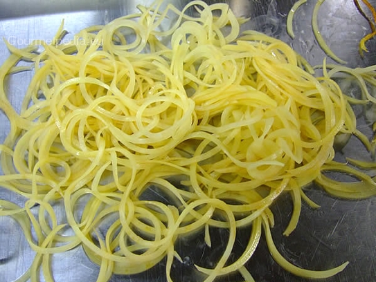 Eine geschälte Kartoffel mit der Spaghettimaschine in dünne lange Streifen schneiden